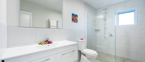 A modern bathroom with a large mirror, white vanity, toilet, and glass shower enclosure.