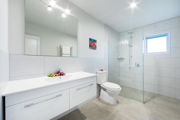 Un baño moderno con un espejo grande, tocador blanco, inodoro y cabina de ducha de vidrio.