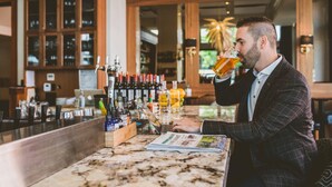 A man in a checkered suit at a bar with a laptop and a magazine on the counter.