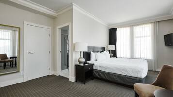 A hotel room with a large bed, a nightstand with lamps, a chair, a TV, and a mirror.