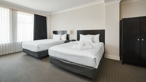 A hotel room with two beds, a wardrobe, and a large window with curtains.