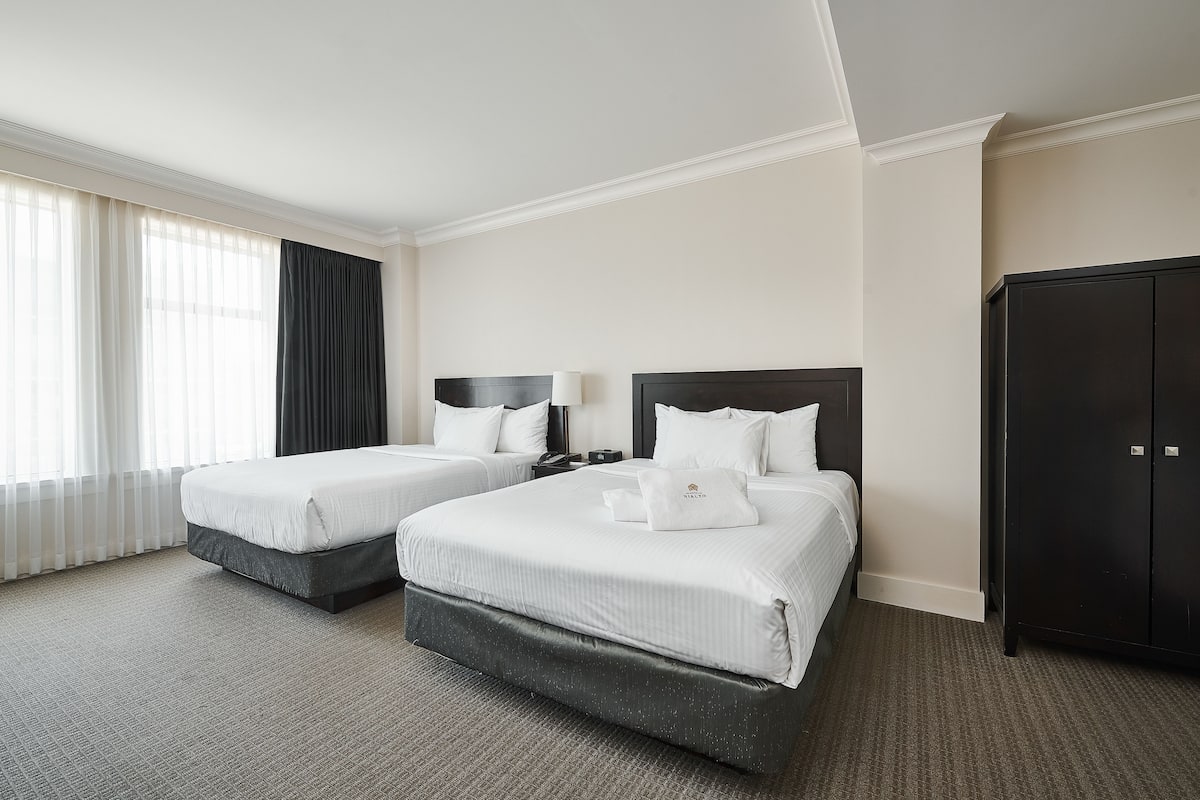 A hotel room with two beds, a wardrobe, and a large window with curtains.