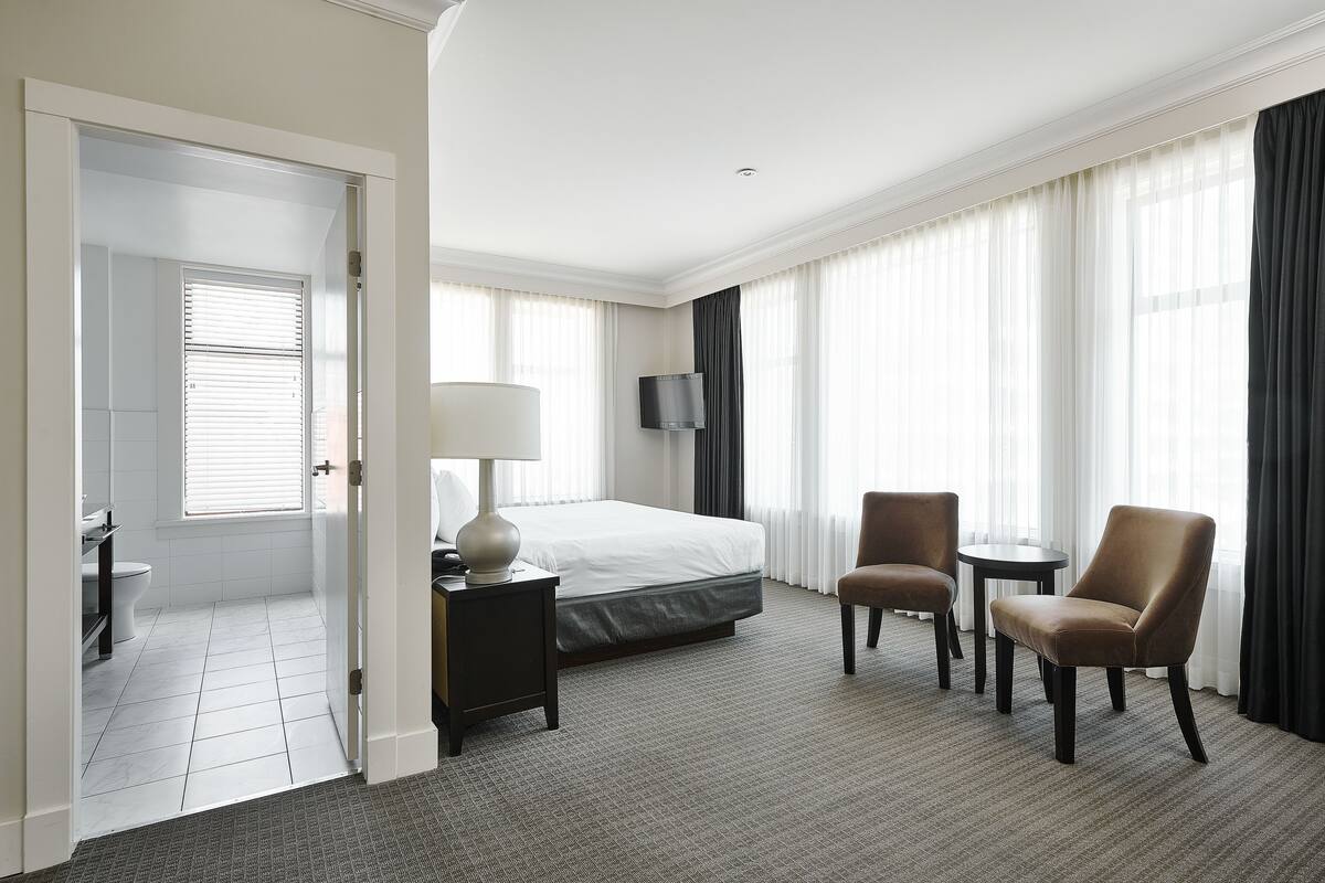 A hotel room with a bed, a desk with a lamp, a chair, a TV, and a window with curtains.