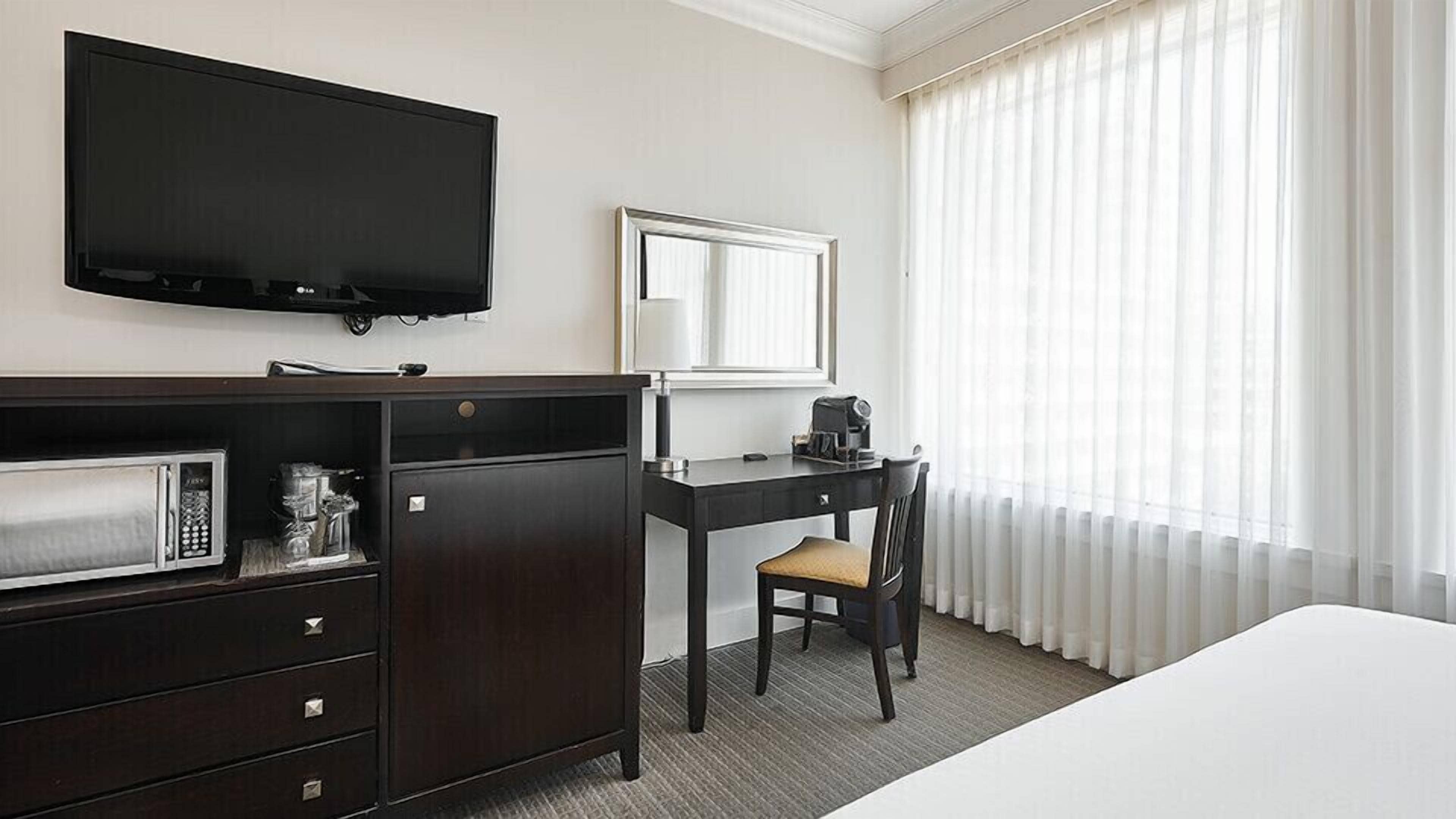 A hotel room with a bed, a desk with a chair, a television, a coffee maker, and a microwave.