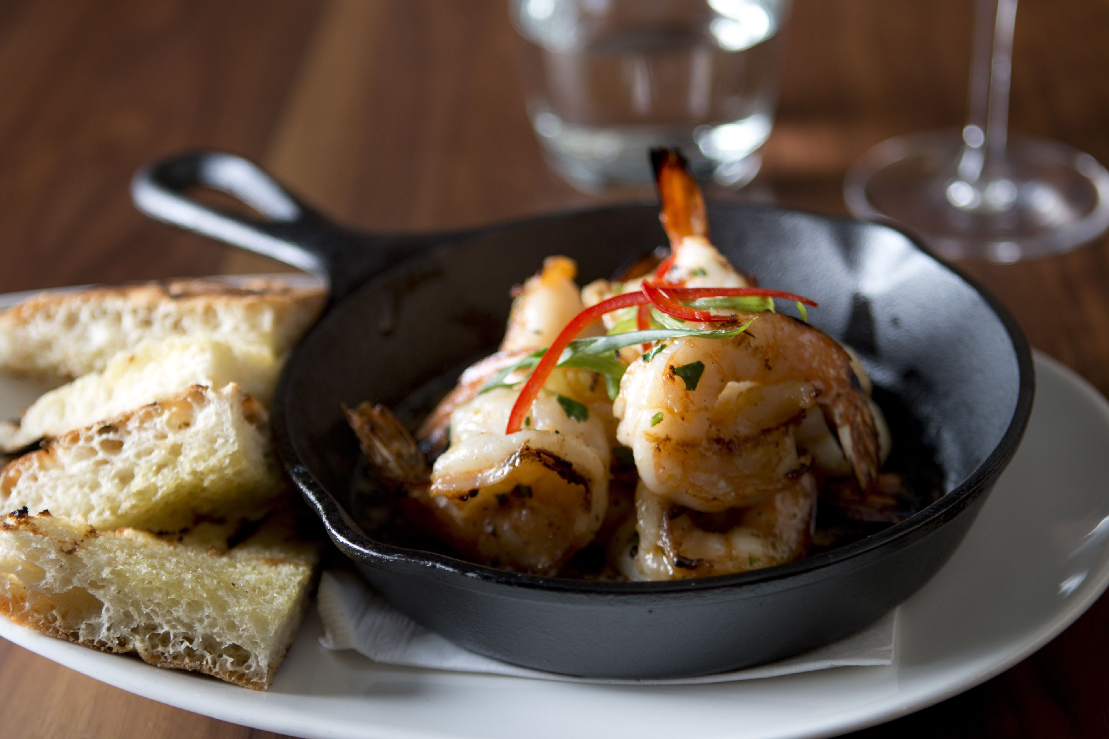 A skillet with grilled shrimp and toasted bread on a plate.