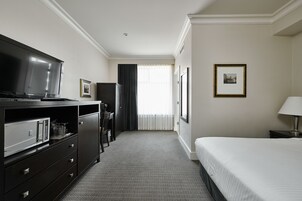 Habitación de hotel con cama, televisor, escritorio y silla, y ventana con cortinas.