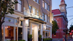 A hotel with a classic facade, large windows, and a prominent clock tower in the background.