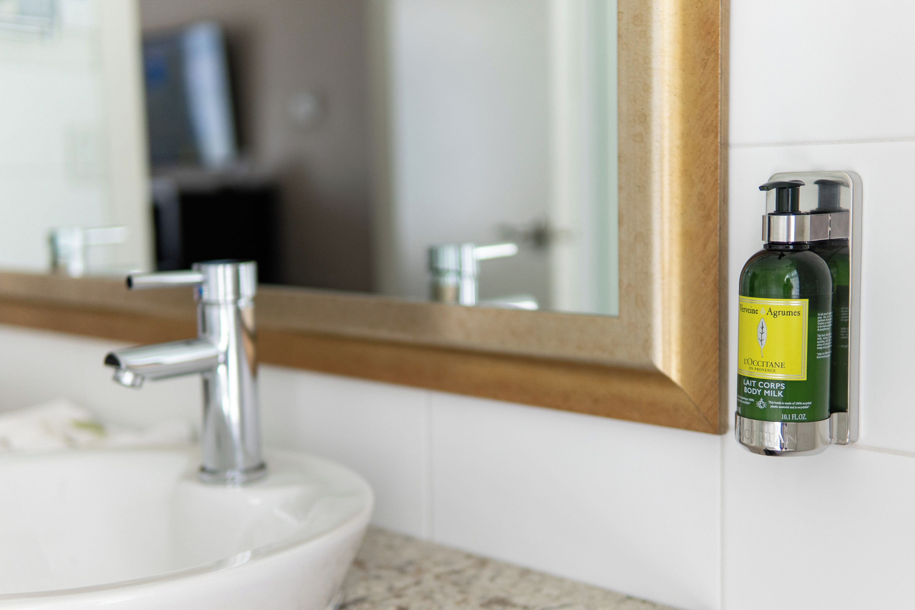 Ein Badezimmerwaschbecken mit einem Chromarmaturen, ein Spiegel mit Holzrahmen und eine Lotionflasche an der Wand.