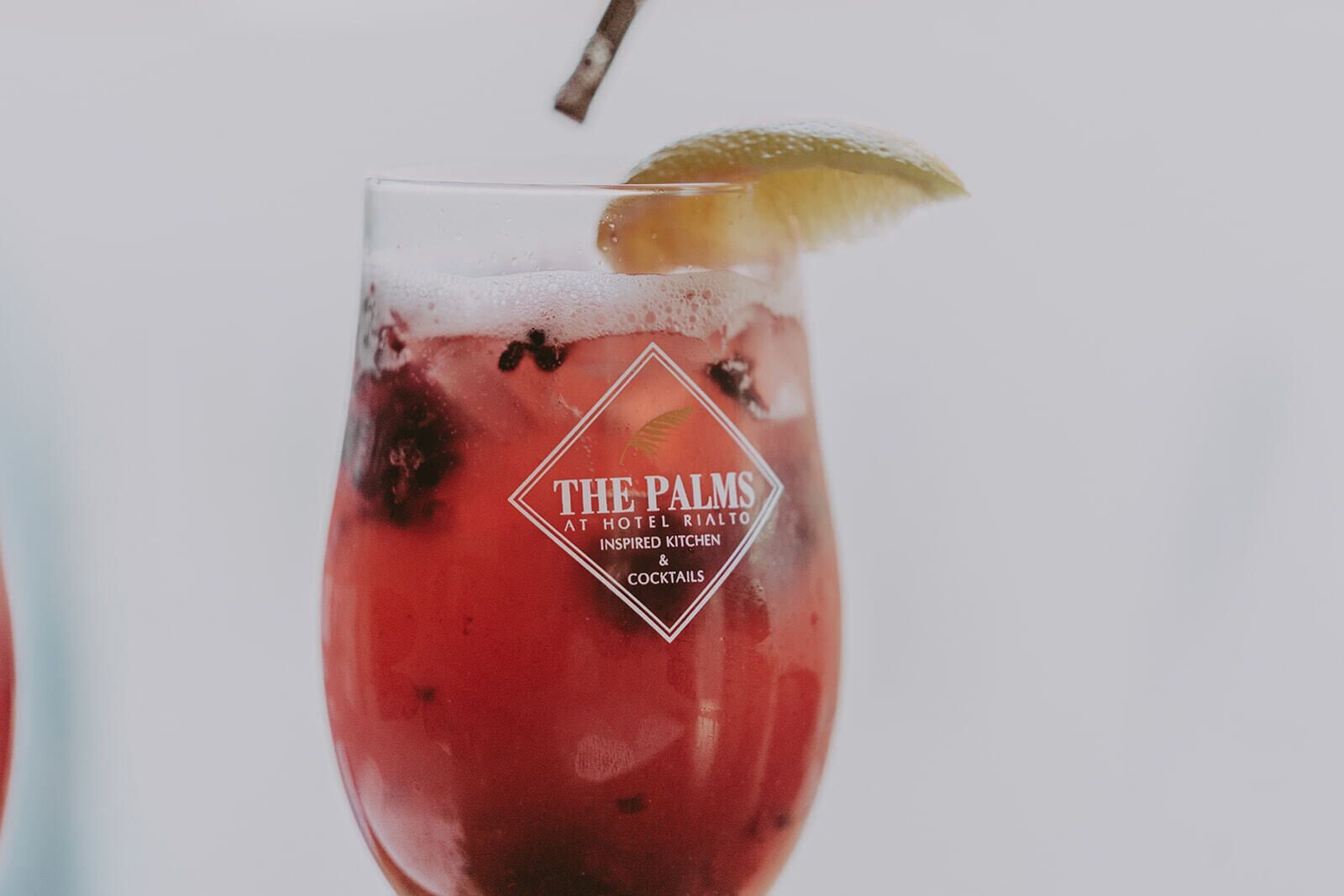 A cocktail glass with a logo and text indicating it is from The Palms at Hotel Rialto, inspired by kitchen and cocktail details.