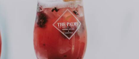 A cocktail glass with a logo and text indicating it is from The Palms at Hotel Rialto, inspired by kitchen and cocktail details.