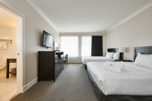 Habitación de hotel con dos camas, un escritorio, una silla, un televisor y una ventana con cortinas.