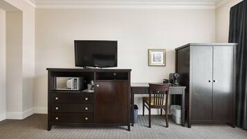 A hotel room with a dark wooden desk, a television, a chair, a cabinet, and a framed picture on the wall.