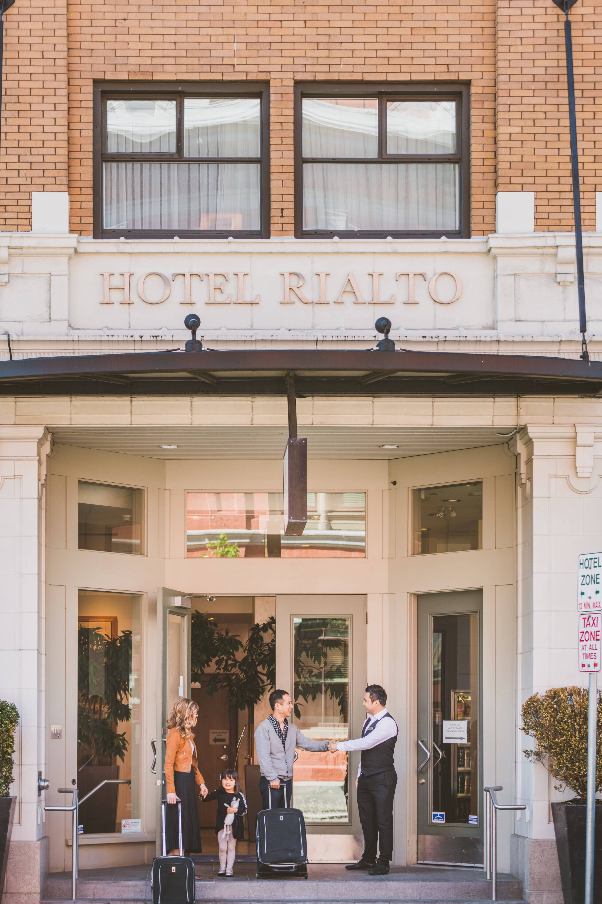 The entrance of Hotel Rialto with a brick facade, a sign above the entrance, and a few people standing outside.