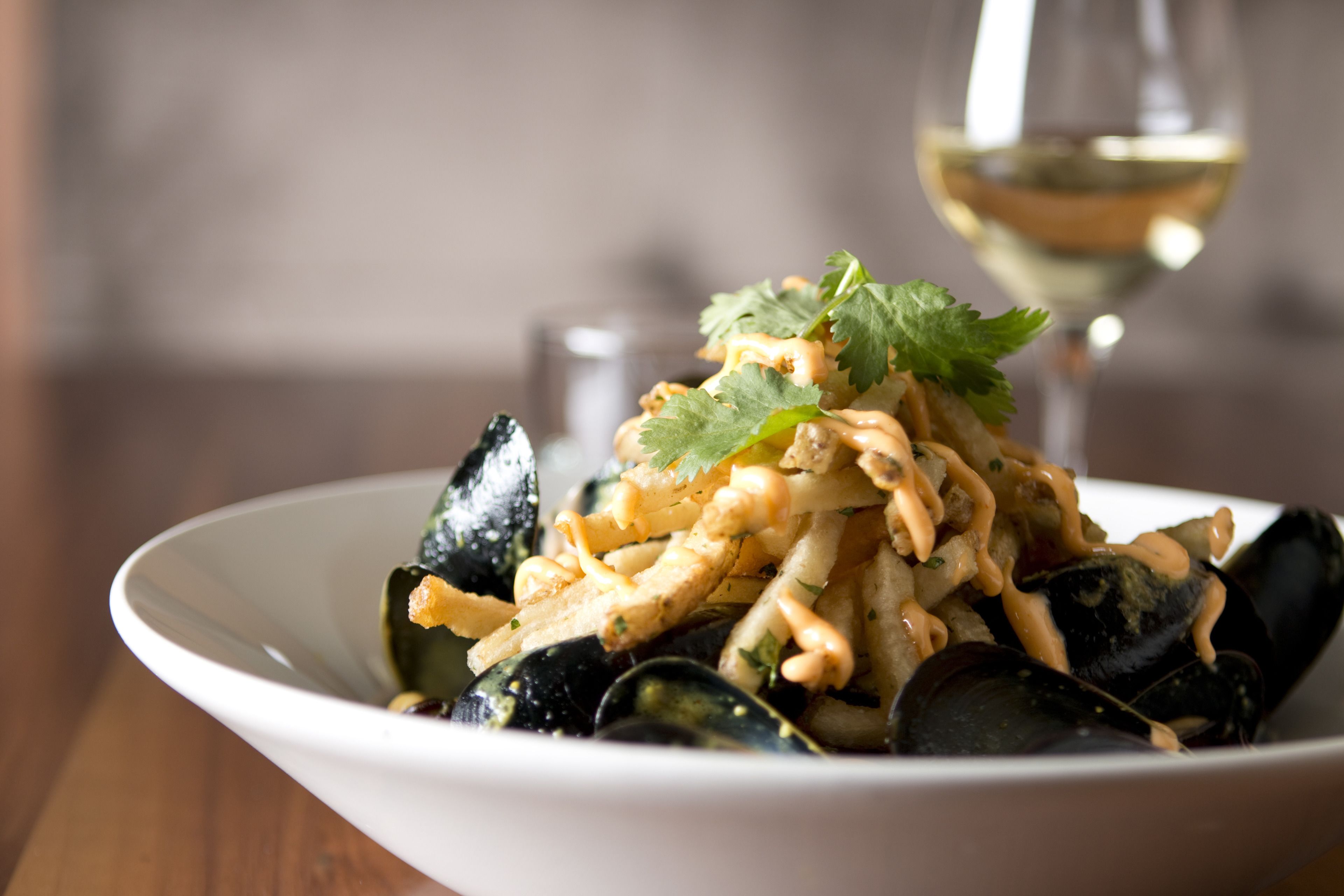 A bowl of mussels with a white wine glass in the background.