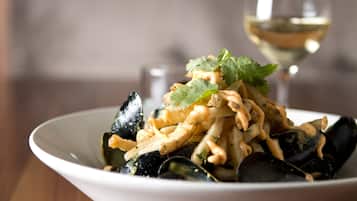 A bowl of mussels with a white wine glass in the background.