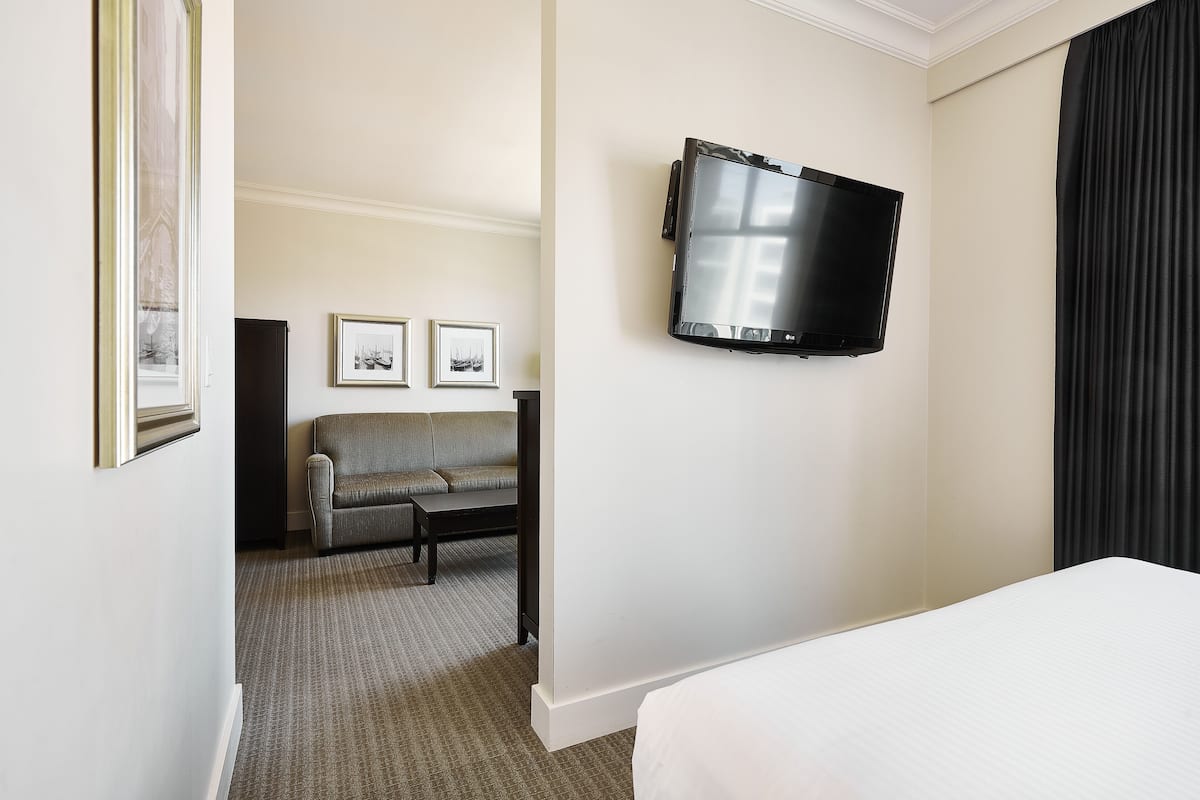 A hotel room with a bed, a TV mounted on the wall, a sofa, and two framed pictures on the wall.