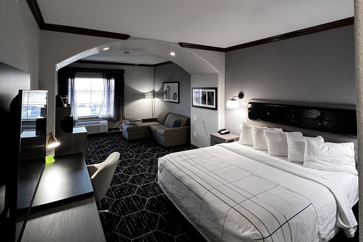 A hotel room with a large bed, a desk, a chair, a TV, and a window with curtains.