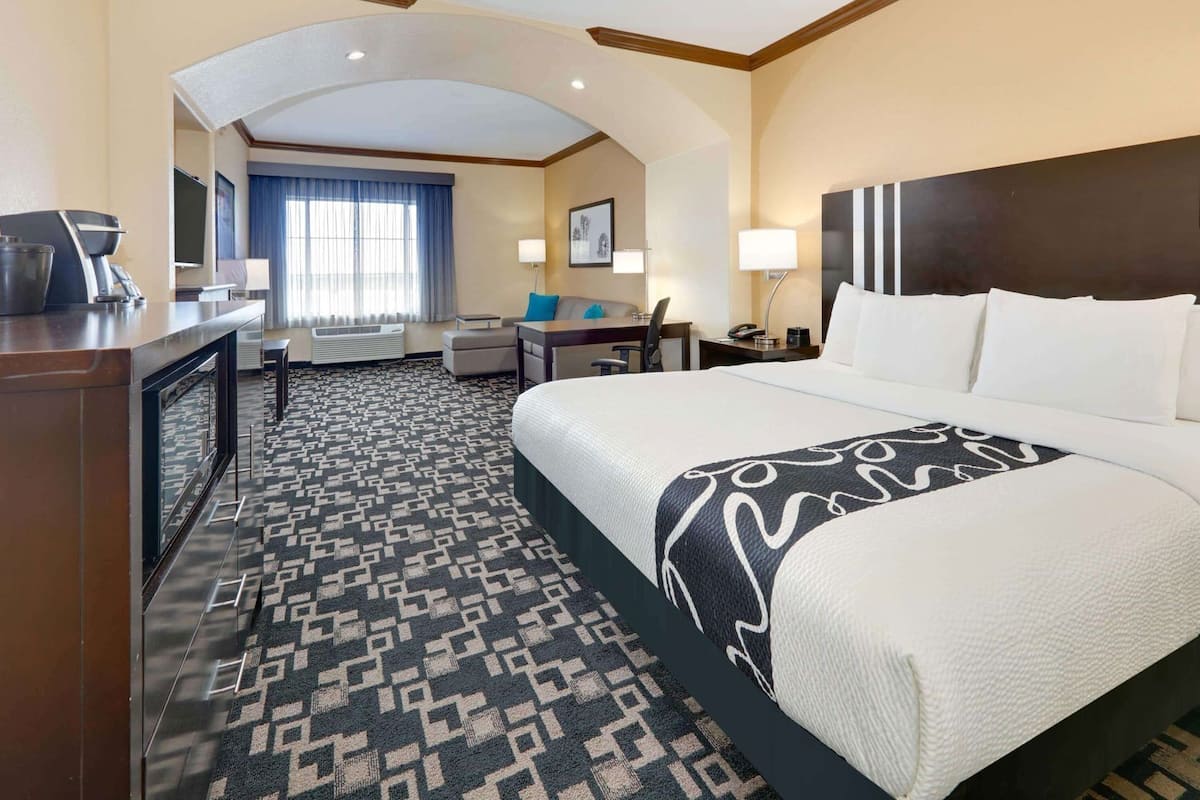 A hotel room with a large bed, a desk, a chair, a coffee machine, and a TV.
