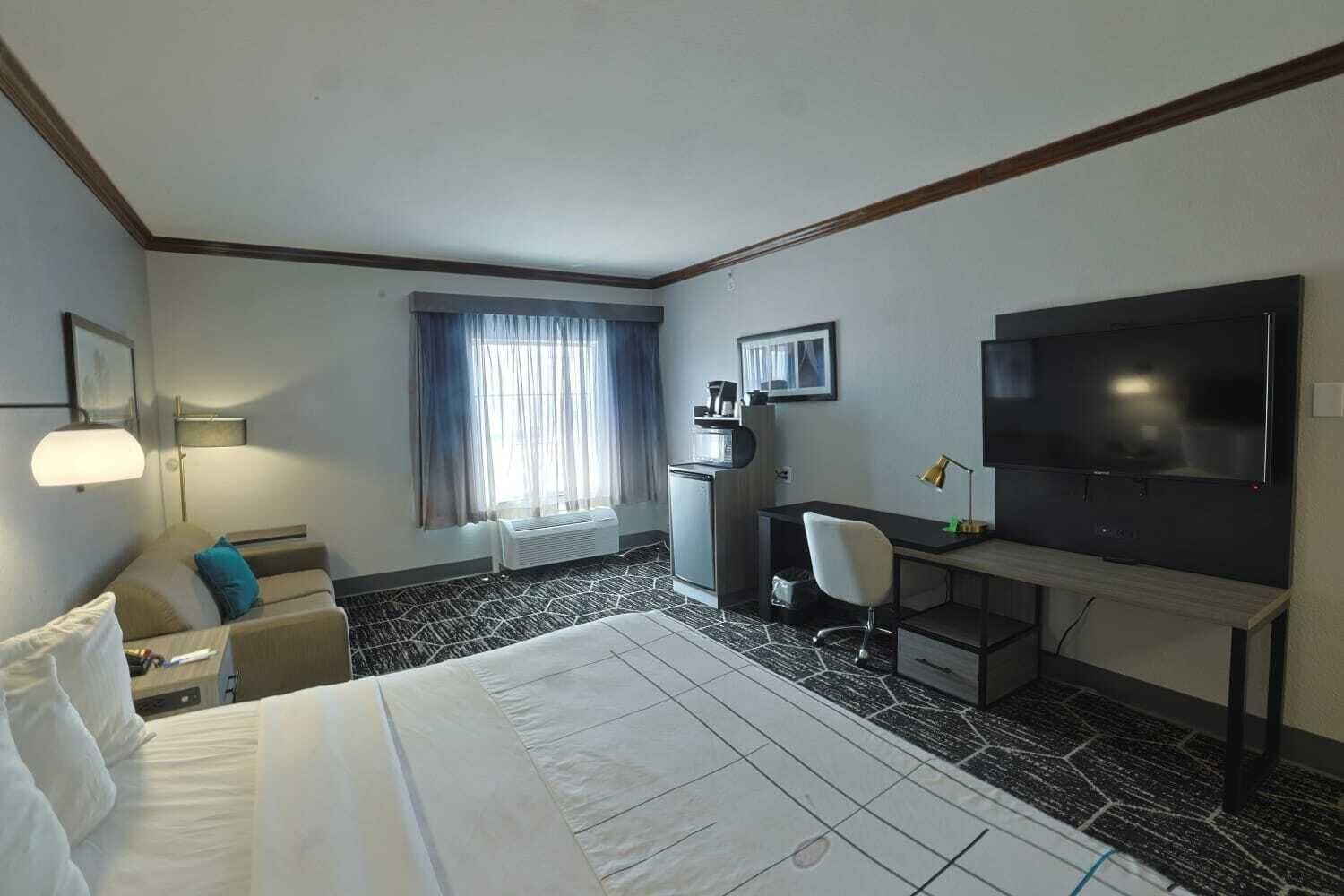 Een hotelkamer met een bed, een bureau, een stoel, een televisie en een raam met gordijnen.