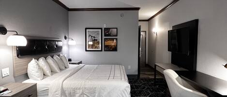 Habitación de hotel con cama, escritorio, silla, televisor y dos cuadros en la pared.