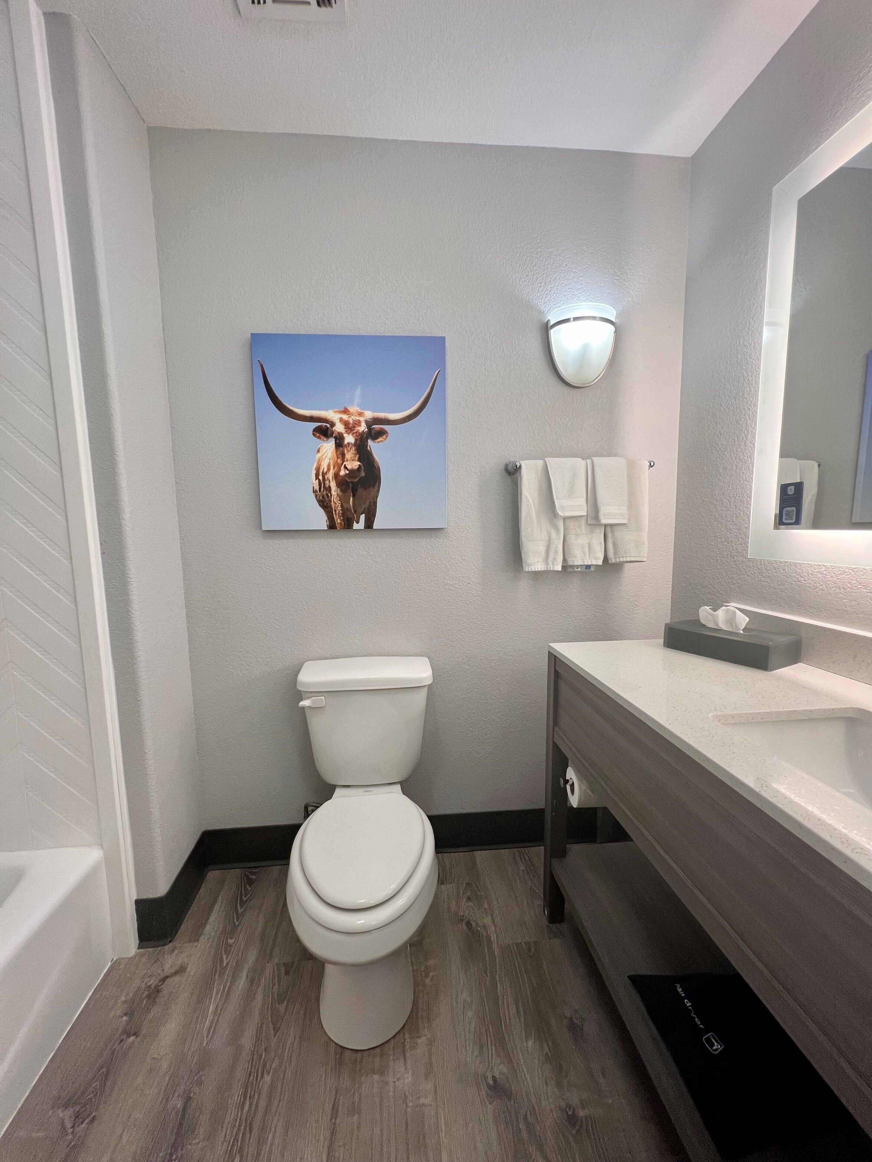 A modern bathroom with a toilet, sink, and a bull-themed artwork on the wall.