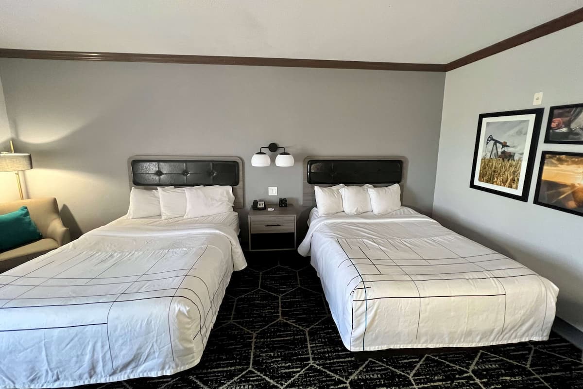 A hotel room with two beds, a nightstand, a lamp, and framed pictures on the wall.