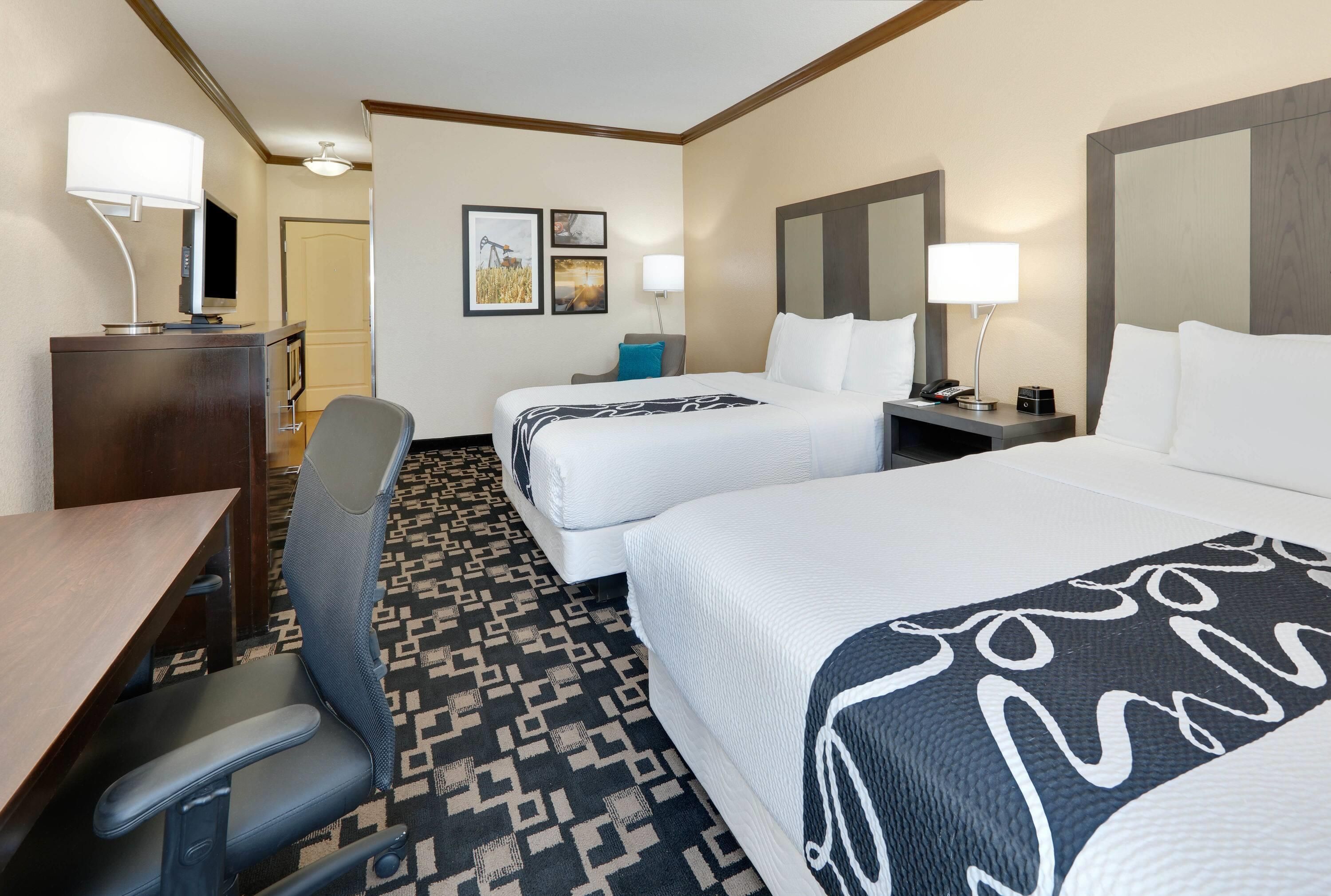 A hotel room with two beds, a desk, a chair, a dresser, and a lamp.