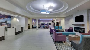 Eine großzügige Lobby mit Empfangstresen, einer Sitzecke mit Sofas und Sesseln, einem an der Wand montierten Fernseher und einem Kamin.
