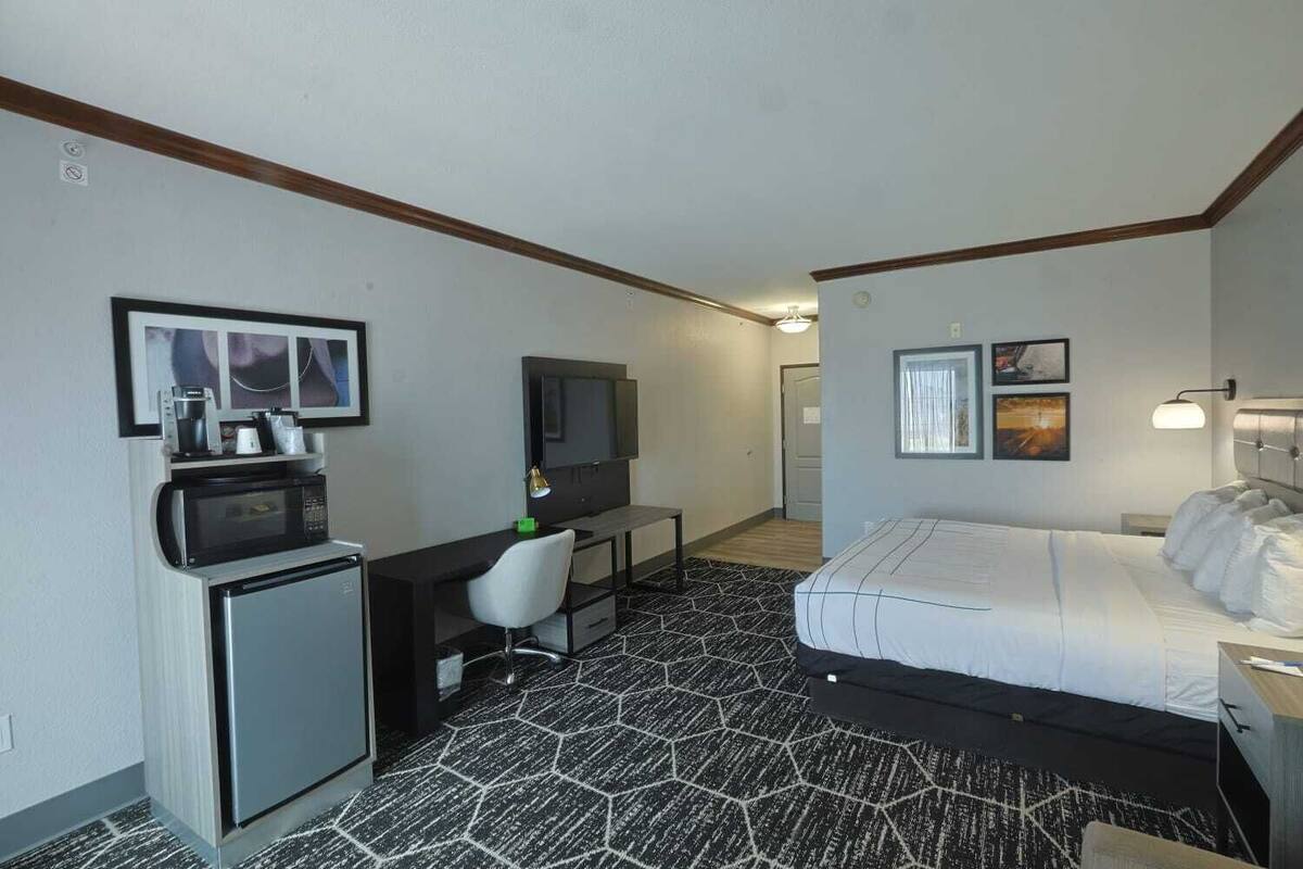 A hotel room with a bed, a desk with a chair, a microwave, a television, and artwork on the walls.