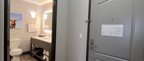 A hallway with a wooden floor, a bathroom with a toilet, sink, and towel rack, and a door with an emergency evacuation plan sign.