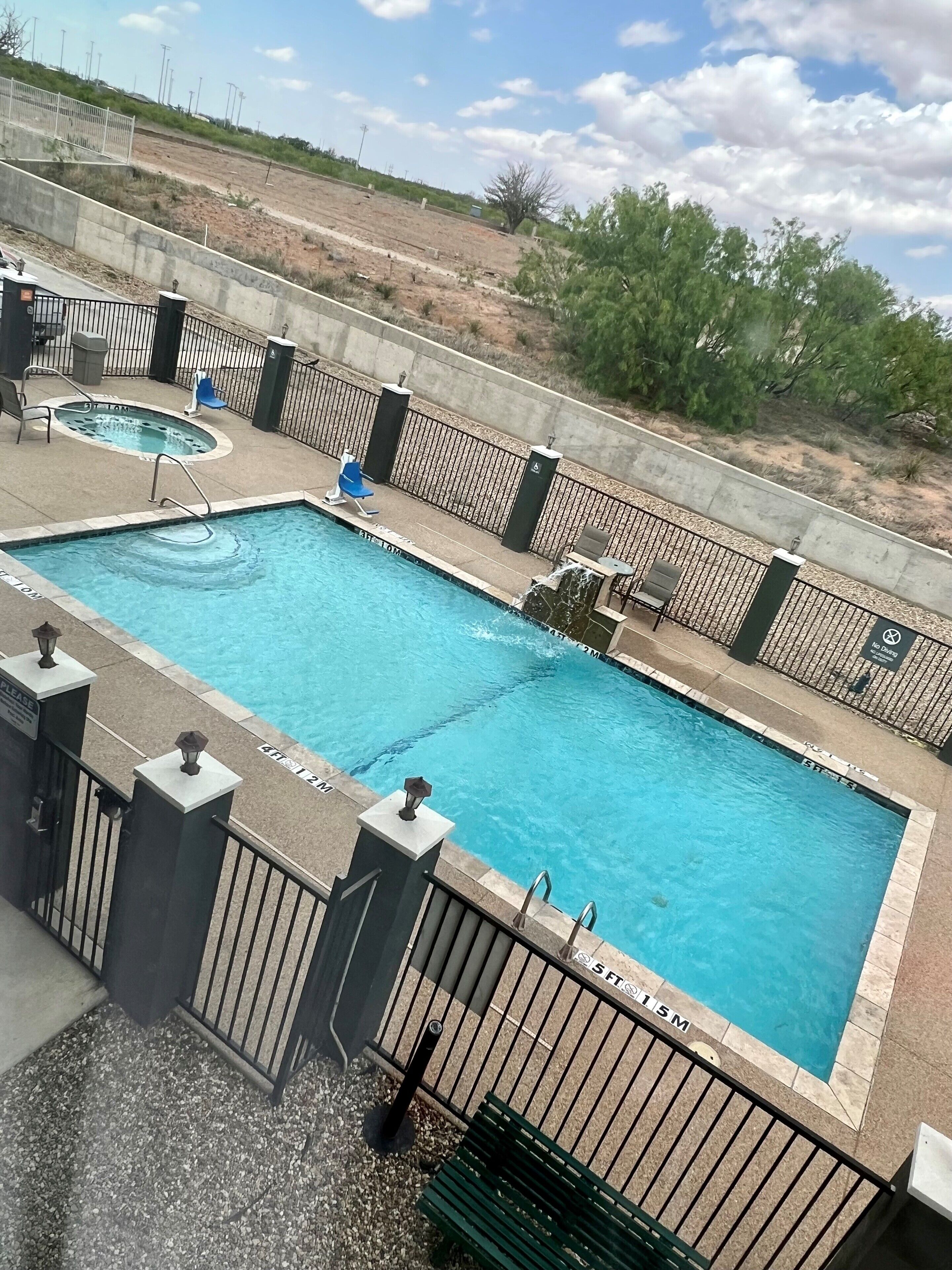 A rectangular swimming pool with a surrounding deck, a hot tub, and a seating area with chairs and a table.