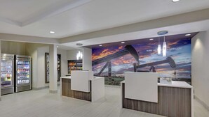 Un espace d’accueil au design moderne, agrémenté d’une grande fresque représentant un coucher de soleil et un pont, de deux comptoirs d’accueil et d’un réfrigérateur rempli de boissons.