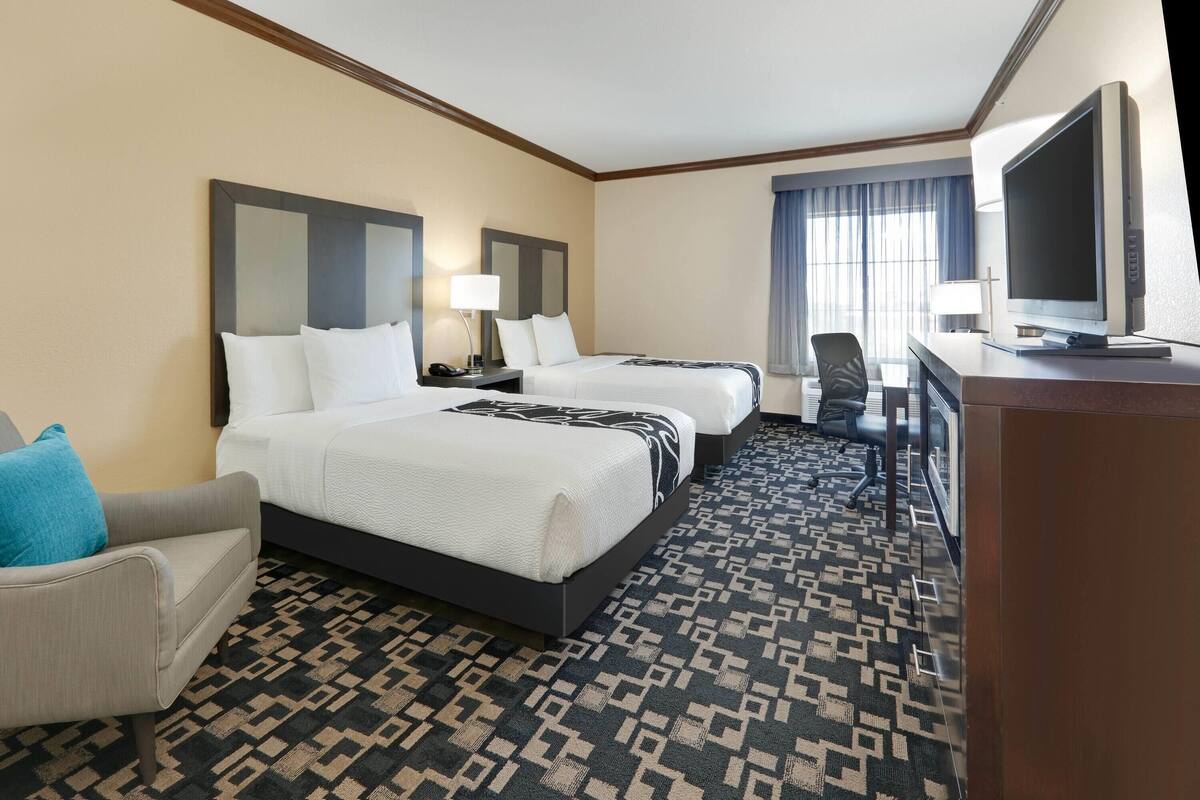 A hotel room with two beds, a desk with a computer, a TV, and a patterned carpet.