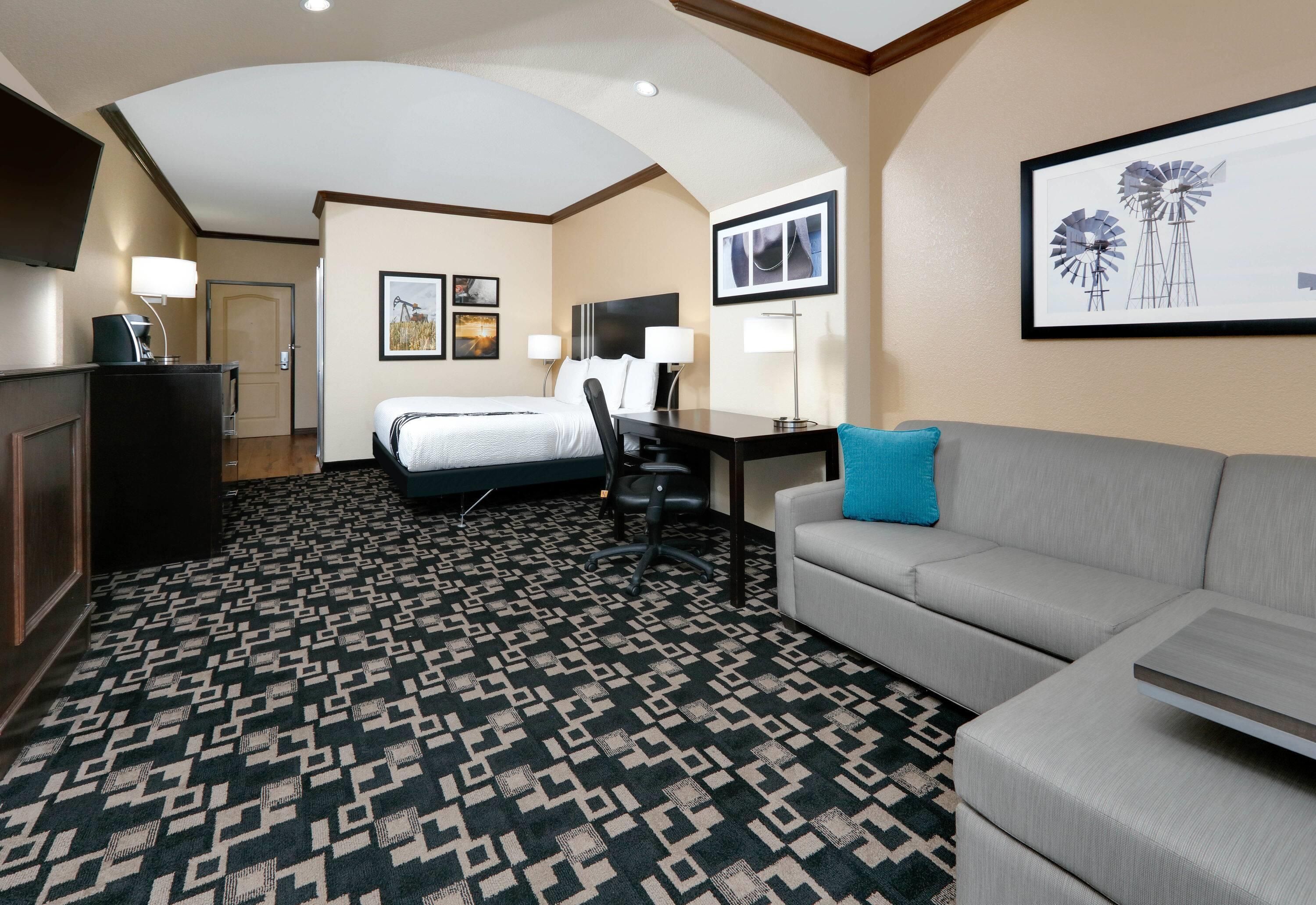 A hotel room with a bed, a desk, a couch, a coffee machine, and a patterned carpet.