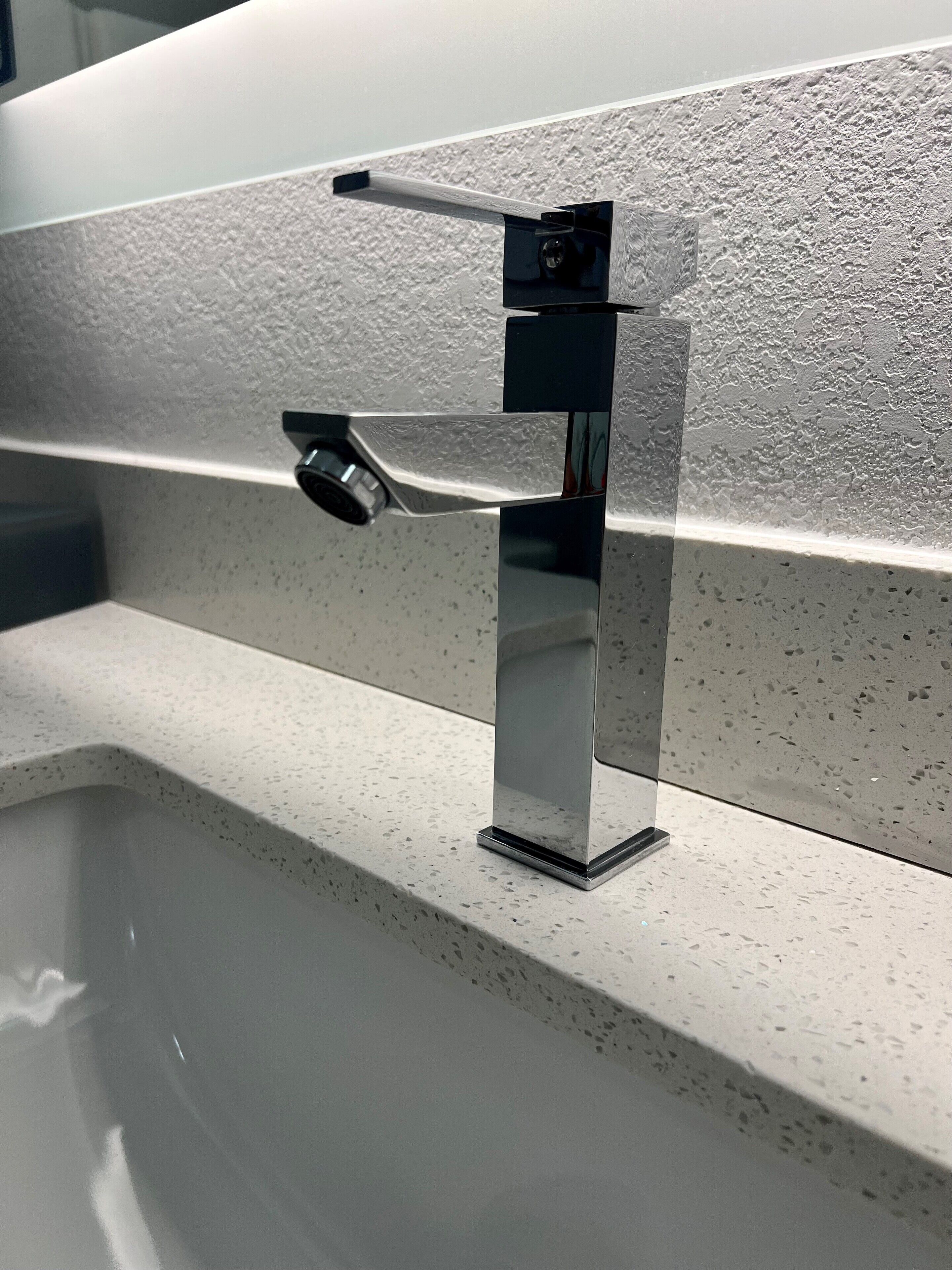 Ein modernes Badezimmer mit einem rechteckigen Waschbecken, einem Chrom-Wasserhahn und einer strukturierten Wand.