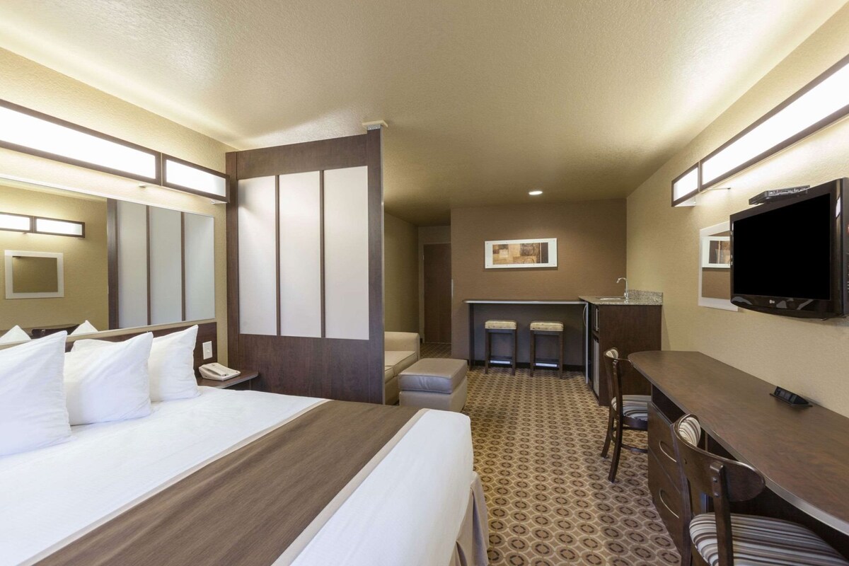 A hotel room with a bed, a desk, a TV, and a small kitchenette.