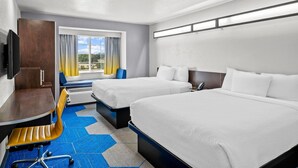 Habitación de hotel con dos camas, un escritorio, una silla, un televisor y una ventana con cortinas.