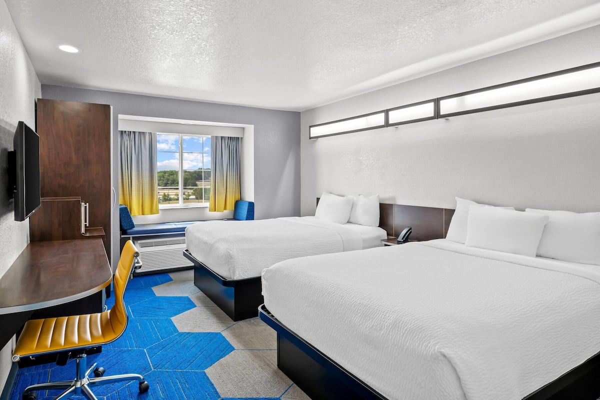 A hotel room with two beds, a desk, a chair, a TV, and a window with curtains.
