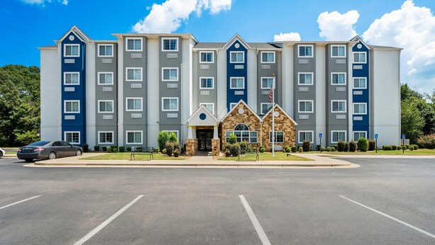 Un hotel de varios pisos con una entrada central, un pequeño edificio de ladrillo y un estacionamiento.