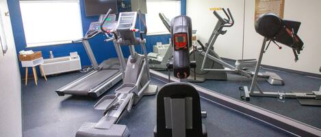 A gym with various exercise equipment, a large mirror, and a window with blinds.
