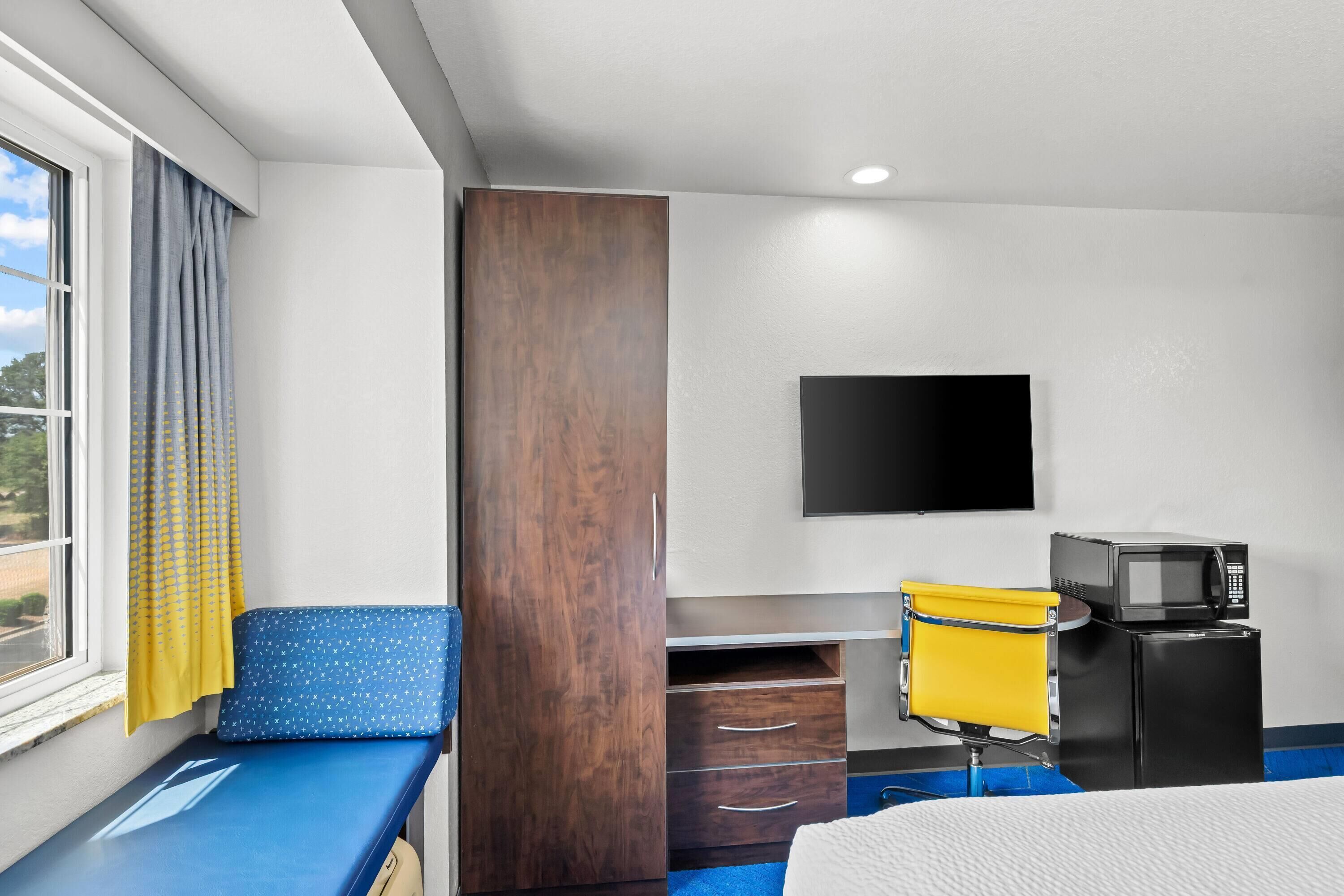 A hotel room with a bed, a desk with a chair, a TV, and a microwave.