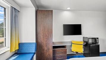 A hotel room with a bed, a desk with a chair, a TV, and a microwave.