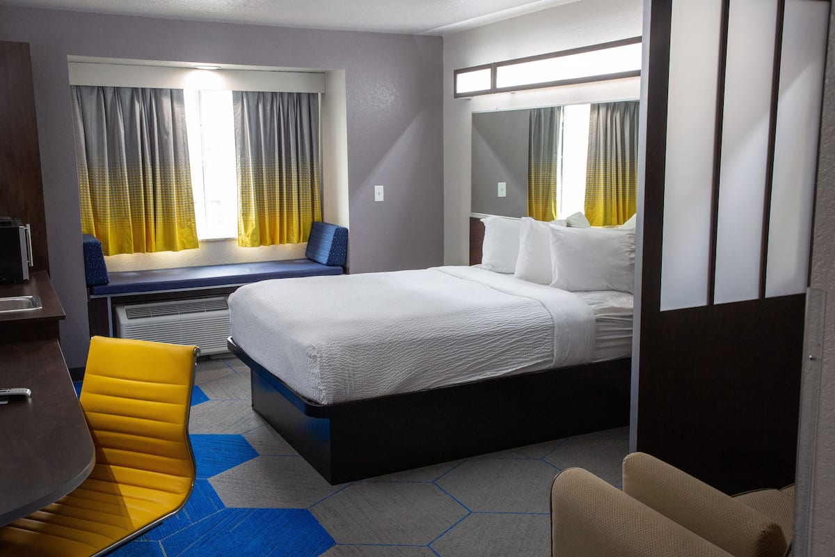 A hotel room with a large bed, a desk, a chair, and a window with curtains.