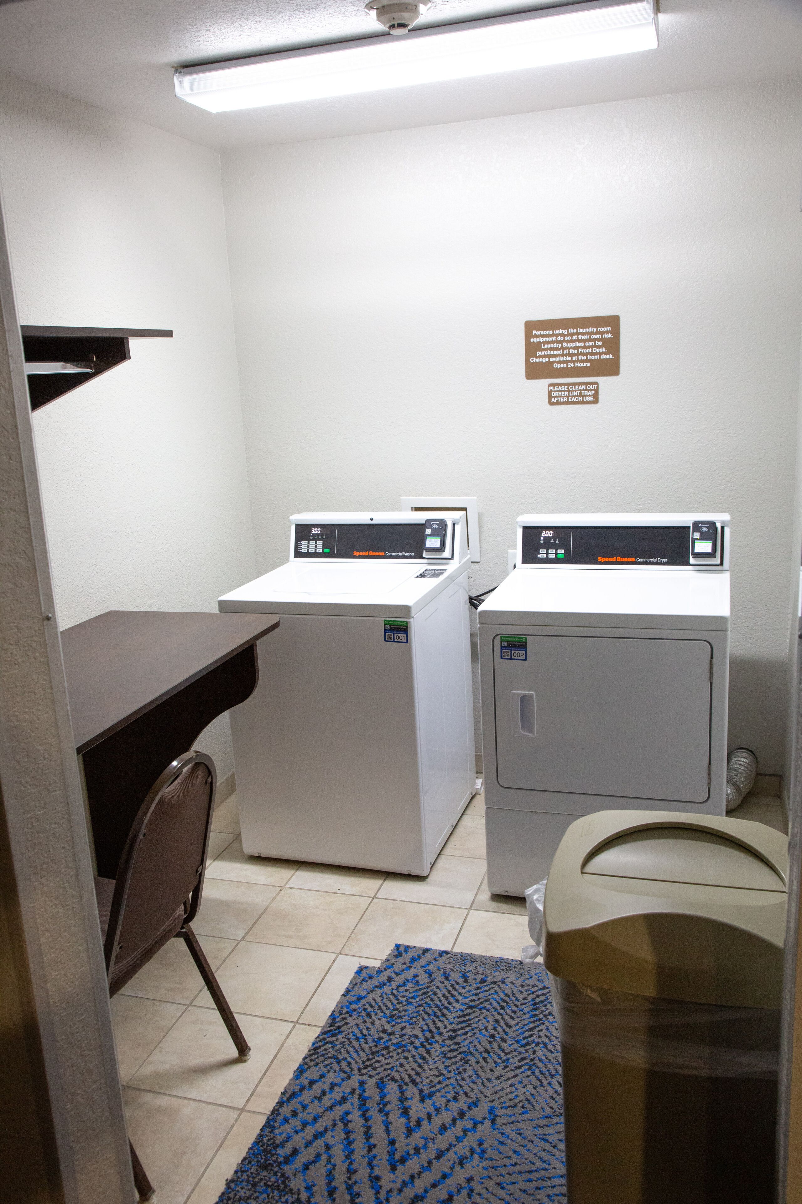 A laundry room with two front-loading washing machines, a small desk, and a chair.