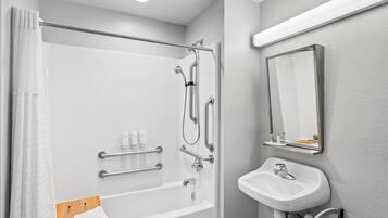 A modern bathroom with a walk-in shower, grab bars, a sink, and a mirror.