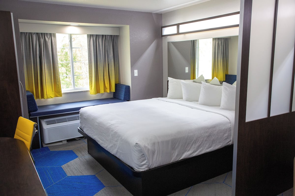 A hotel room with a large bed, a window with curtains, a desk, and a chair.