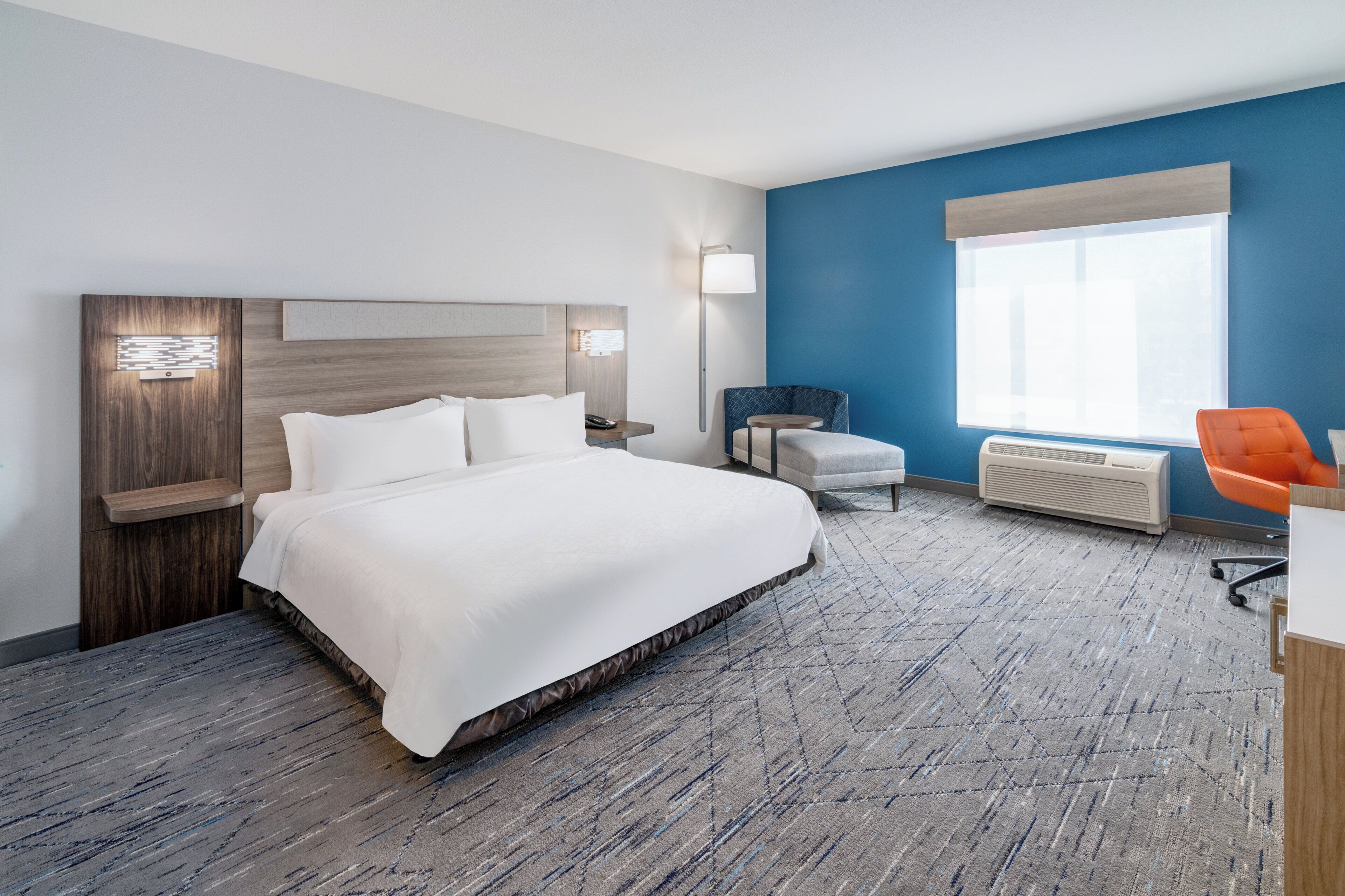 Een hotelkamer met een groot bed, een bureau, een oranje stoel, een raam en een wandradiator.
