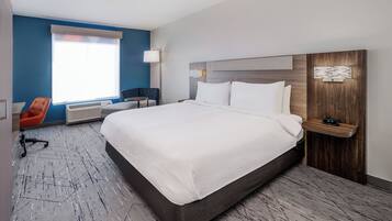 Una habitación de hotel con una cama grande, un escritorio, una silla, una ventana con persianas y un reloj en la pared.