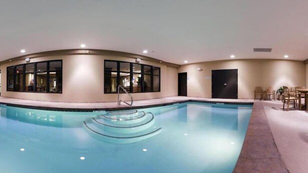 Una amplia piscina cubierta con agua cristalina, rodeada por una pared color beige con grandes ventanales.