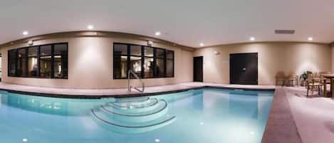 A large indoor swimming pool with clear water, surrounded by a beige wall with large windows.